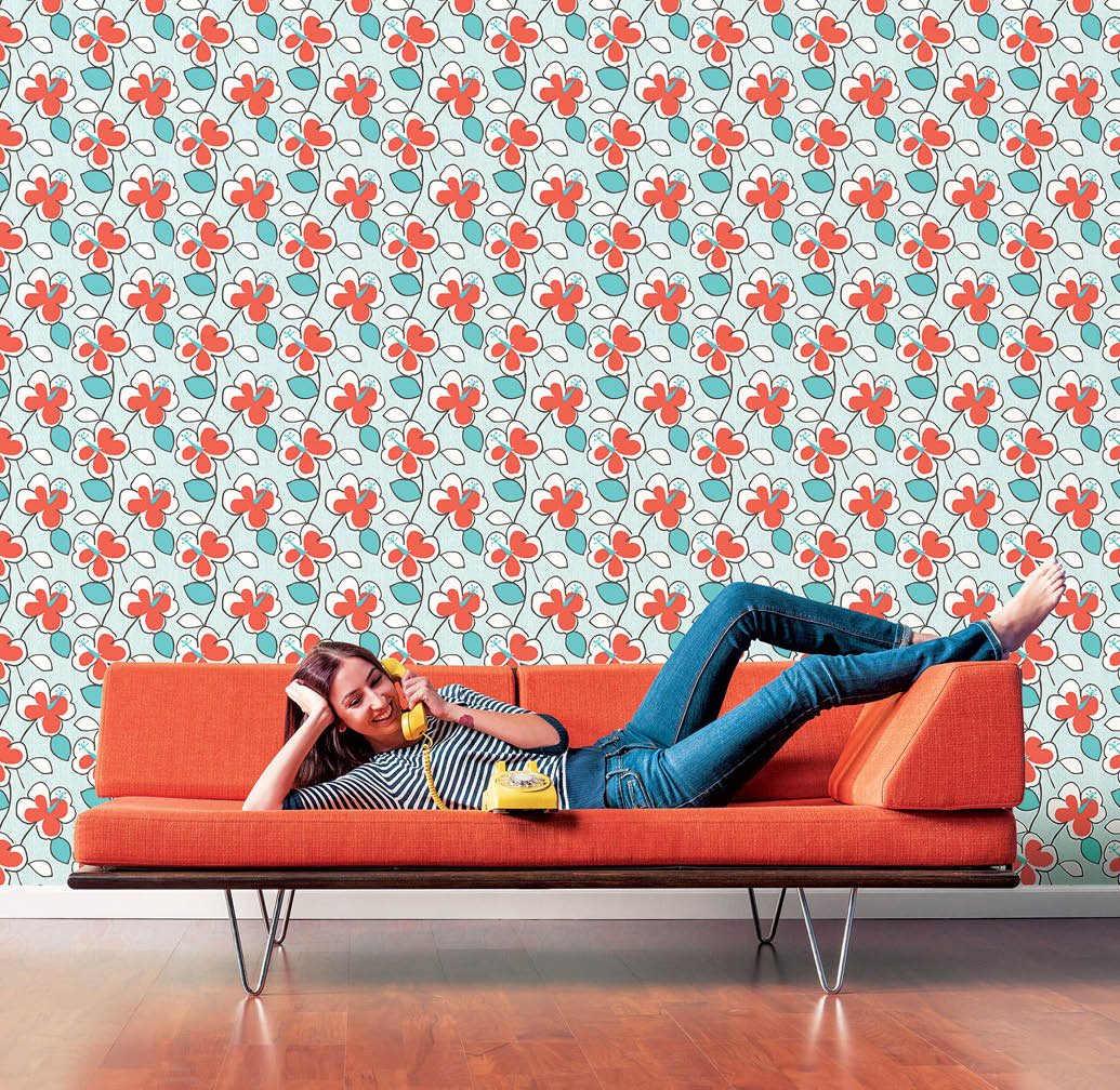Young woman with long brown hair in her early twenties lying down on a mid-century  modern couch and talking on a yellow rotary vintage telephone with mid century floral design in teal and orange